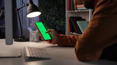 Ofis çalışanı fazla mesai yapıyor. Genç iş adamı gece geç saatlere kadar ofiste çalışıyor. Krom anahtar yeşil ekran arka planlı akıllı telefonu kaydırıyor. Çalışma alanı modeli..