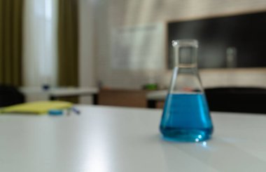 Ekipman ve mobilyalarla dolu üniversite odası. Masaları, sandalyeleri ve tahtası olan boş bir kimya sınıfı. Eğitim ve öğretim için çalışma alanı. Masanın üzerinde mavi sıvı bulunan cam şişe, kapat..