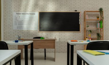 Ekipman ve mobilyalarla dolu üniversite odası. Masaları, sandalyeleri ve tahtası olan boş bir kimya sınıfı. Eğitim ve öğretim için çalışma alanı. Masalardaki defterler, duvardaki periyodik tablolar.