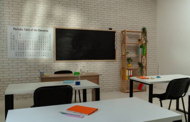Ekipman ve mobilyalarla dolu üniversite odası. Masaları, sandalyeleri ve tahtası olan boş bir kimya sınıfı, çalışmak için çalışma alanı. Masalarda defterler ve şişeler, duvarlarda periyodik tablolar.