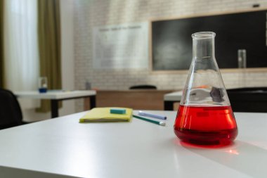 Ekipman ve mobilyalarla dolu üniversite odası. Masaları, sandalyeleri ve tahtası olan boş bir kimya sınıfı. Eğitim ve öğretim için çalışma alanı. Masada kırmızı sıvı bulunan cam şişe, yakın görüş..