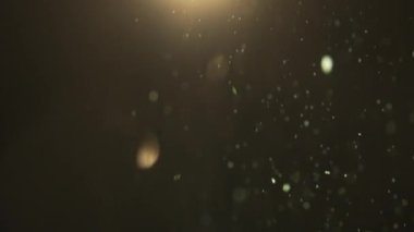 Minik kıvılcımlar havada rastgele uçuşuyor, nesneler için boş uzay şablonu. Pek çok parlak yeşil parıltı, yukarıdan gelen ışıkla boş arka planda süzülüyor. Yakın çekim.