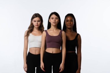 Stüdyoda bir grup çok ırklı model var. Beyaz stüdyo arka planında izole edilmiş, kendinden emin bir ifadeyle kameraya poz veren üç pozitif çok ırklı genç kadın. Çok kültürlü güzellik kavramı.