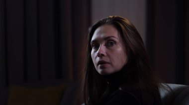 Karanlık dairede stresli bir kadın. Akıl sağlığıyla ilgili sorunları olan bir kadın, battaniyeyle kaplı bir kanepede oturuyor, depresif bir ifade, korkmuş bir yüzle etrafına bakıyor, yakından bakıyor..