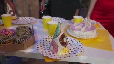 Partideki gençler. Ergenlerin doğum günü partisi, kızlar ve erkekler atıştırmalık masasının etrafında donutlar, pizzalar, içkiler ve şenlikli pastalarla bekliyor. Mutlu bir grup genç birlikte eğleniyor. Yavaş çekim.