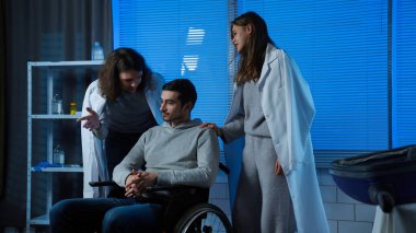 Hasta erkek hasta klinik koğuşunda dinleniyor. Hastanedeki yetişkin hasta taburcu olmaya hazır. Tekerlekli sandalyede oturuyor ve konuşuyor. Arkadaşları, gülümseyen ve dinleyen adamı destekliyor..