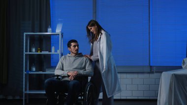 Hasta erkek hasta klinik koğuşunda dinleniyor. Hastanedeki yetişkin hasta taburcu olmaya hazır. Tekerlekli sandalyede oturuyor. Kadın arkadaşı omzunu destekliyor ve hafifçe vuruyor..