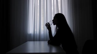 Karanlıkta odada yalnız bir kadın. Pencerenin önündeki masada oturan, bir bardak su içen, şüpheyle düşünen, karar veren bir kadın silueti. İnsan duyguları ve akıl sağlığı. Yavaş çekim.