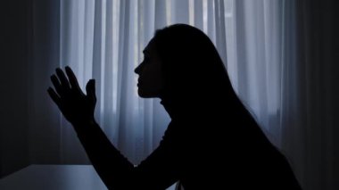 Karanlıkta odada yalnız bir kadın. Pencerenin önündeki masada oturan bir kadın silueti, hayal kırıklığına uğramış ifade, zihinsel kriz, bitkin düşmüş ruh hali. İnsan duyguları ve akıl sağlığı.