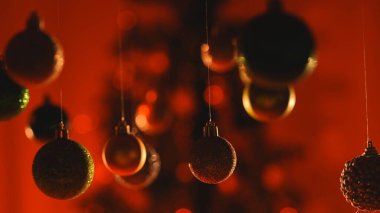 Yeni yıl dekorasyonları. Kırmızı turuncu ışık altında Noel ağacı topları, tepesinden sarkan parlak renkli oyuncaklar, şenlikli arka planda yakın plan süsleri..