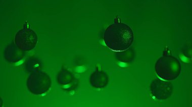 Yeni yıl dekorasyonları. Noel ağacı altın topları, yukarıdan sarkan yeşil neon ışıklarıyla vurgulanmış, ışıltılı süsler, bulanık arka plandaki çelenkler..