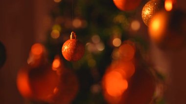 Yeni yıl dekorasyonları. Kırmızı turuncu ışık altında Noel ağacı topları, tepesinden sarkan parlak renkli oyuncaklar, ışıldayan süsler yakın çekim, bulanık arka plan şenliği..