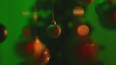 Yeni yıl dekorasyonları. Noel ağacı yeşil topları, yeşil ışıkla vurgulanmış, süsleri ışıldıyor, şenlikli arka planda yakın plan çekimleri yapılıyor..