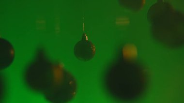 Yeni yıl dekorasyonları. Noel ağacı topları, yukarıdan sarkan parlak renkli oyuncaklar yeşil ışıkla aydınlatılan dumanlar, şenlikli arka planda belirginleşen süsler..