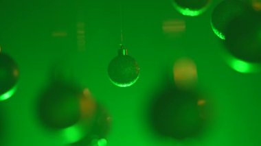 Yeni yıl dekorasyonları. Noel ağacı altın renkli toplar, tepeden sarkan yeşil neon ışıklarıyla vurgulanmış, ışıltılı süsler, şenlikli arka planda yakın çekim çelenkler..