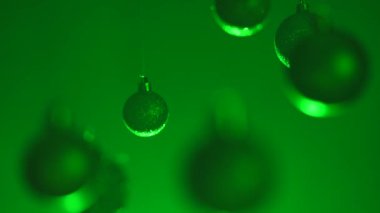 Yeni yıl dekorasyonları. Noel ağacı altın renkli toplar, tepeden sarkan yeşil neon ışıklarıyla vurgulanmış, ışıltılı süsler, şenlikli arka planda yakın çekim çelenkler..