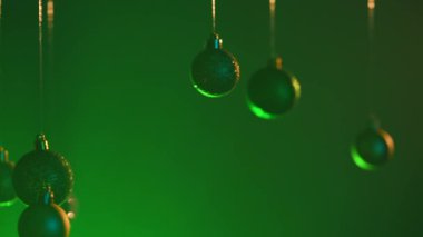 Yeni yıl dekorasyonları. Noel ağacı altın topları, yukarıdan sarkan yeşil neon ışıklarıyla vurgulanmış, ışıltılı süsler, bulanık arka plandaki çelenkler..