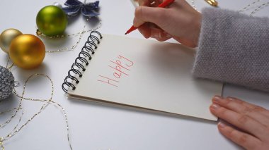 Yeni yıl kararı ve dilek listesi. Noel 'in yakın çekimleri, dekore edilmiş beyaz masa, not defteriyle süslenmiş kadın el yazısı, sarmal defterle yazılmış yeni mutlu 2025 için selamlama, üst görünüm..