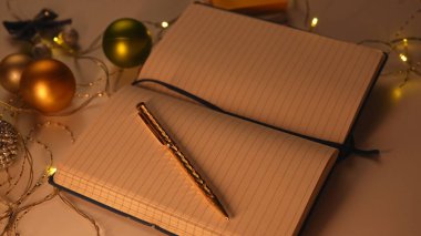 Yeni yıl kararı ve dilek listesi. Noel dekore edilmiş ofis masasının yakın çekimi, boş sayfası ve masasında duran kalemle birlikte açık bir defter, metin eklemek için boşluk, üst görünüm.