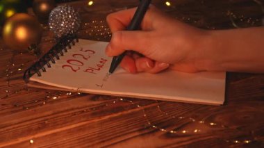 Yeni yıl kararı ve dilek listesi. Noel 'in yakın çekimleri ahşap masa, yeni yıl için kalemle yazı yazan kadın, aşk, mutluluk ve parayla numaralandırma listesi..