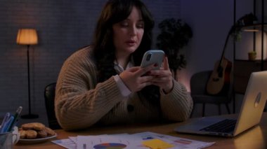 Evden uzakta bağımsız bir iş. Genç iş kadını ofis kumandasında geç saatlere kadar çalışıyor, akıllı telefona kayıyor, patrondan korkuyor, dizüstü bilgisayarda yazmaya devam ediyor. Yan çekim.