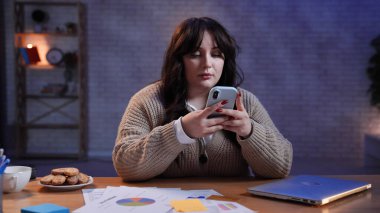 Evden uzakta bağımsız bir iş. Genç iş kadını serbest çalışan masa başında oturuyor ev ofisinin kumandasında geç saatlere kadar çalışıyor, akıllı telefondan mesaj atıyor, sosyal medyayı karıştırıyor..