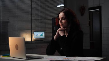 Ofiste çalışan bir iş adamı. Genç iş kadını geç saatlere kadar masa başında çalışır, dizüstü bilgisayar kullanır, monitöre bakar, kafa kafaya tutuşmayı düşünür, olumlu ifade, orta çekim.