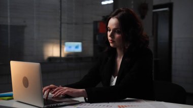 Ofiste çalışan bir iş adamı. Genç iş kadını geç saatlere kadar masa başında çalışır, dizüstü bilgisayar kullanır, klavyeye yazar, odaklanmış ifade, kenar çekim.