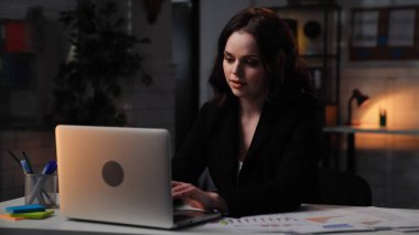 Ofiste çalışan bir iş adamı. Genç iş kadını geç saatlere kadar masa başında çalışır, dizüstü bilgisayar kullanır, klavyeye yazar, odaklanmış olumlu ifade, yan çekim....