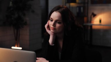 Ofiste çalışan bir iş adamı. Genç iş kadını geç saatlere kadar masa başında çalışır, dizüstü bilgisayar kullanır, monitöre bakar, el pozitifliğine kafa tutar, yakın çekim yapar..