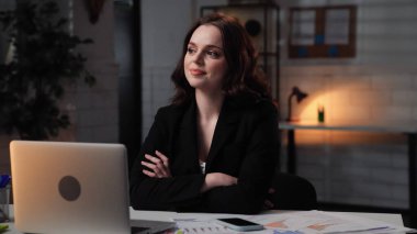 Ofiste çalışan bir iş adamı. Genç iş kadını geç saatlere kadar masa başında oturuyor, dizüstü bilgisayar kullanıyor, ellerini çapraz yapıyor, tatmin olmuş bir ifade sergiliyor..