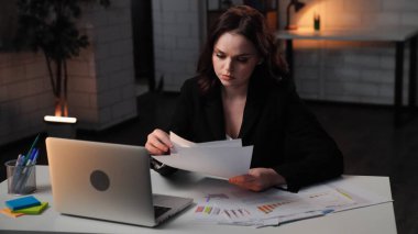 Ofiste çalışan bir iş adamı. Genç iş kadını geç saatlere kadar masa başında çalışır, dizüstü bilgisayar kullanır, belgeler okur, ciddi odaklı ifade, orta çekim.