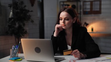 Ofiste çalışan bir iş adamı. Genç iş kadını geç saatlere kadar masa başında oturur, dizüstü bilgisayara bakar, elinde banka kartı, odaklanmış ifade, orta çekim.
