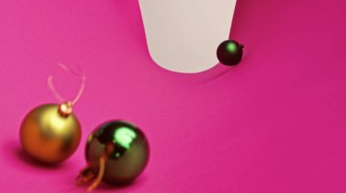 Yeni yıl dekorasyonları. Noel ağacı altın ve yeşil parıldayan toplar, parlak renkli süs oyuncakları parlak pembe kağıt arka planda yuvarlanıyor.