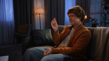 Adam evde boş vakit geçiriyor. Genç bir adam akşamını evde, oturma odasında elinde bozuk para, üzgün, hayal kırıklığına uğramış umutsuz bir ifadeyle oturarak geçiriyor..