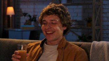 Adam evde boş vakit geçiriyor. Genç adam akşamını evde, oturma odasında kanepede oturup televizyon izleyerek meyve suyu içerek geçiriyor..