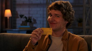 Adam evde boş vakit geçiriyor. Genç adam akşamını evinde, oturma odasında koltukta oturup elinde altın kredi kartı tutarak mutlu bir şekilde gülümseyerek, mutlu bir ifadeyle, kapatarak geçirir..