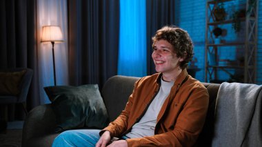 Adam evde boş vakit geçiriyor. Genç bir adam akşamını evde kanepede oturup televizyon izleyerek, film ya da haber programıyla, gülümseyen bir ifadeyle geçirir..