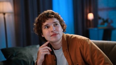 Adam evde boş vakit geçiriyor. Genç bir adam akşamını evde, oturma odasında kanepede oturup televizyon izleyerek, akşam film haber programlarıyla, gülümseyen bir ifadeyle, yakın çekim yaparak geçirir..