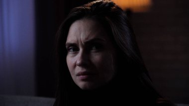 Karanlık dairede depresif bir kadın. Akıl sağlığı bozuk bir kadın silueti, koltukta oturuyor, depresif bir ifade, etrafa bakıyor, kızgın bir yüz, yakın çekim.