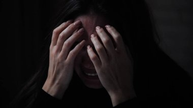 Karanlık dairede depresif bir kadın. Ruhsal sorunları olan bir kadın silueti, koltukta oturuyor, depresif bir ifade, ağlayan bir kalp, elleri kapalı bir yüz, yakın çekim.