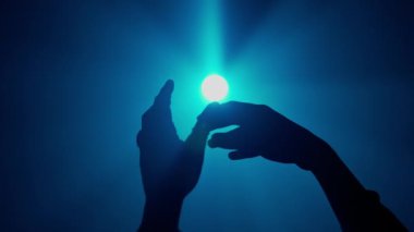 El hareketleri ve işaretleri. El silueti el hareketlerini gösteriyor. Avuç içlerini bir arada tutan parlak mavi spot ışıkları stüdyonun arka planında izole edilmiş. Yakın plan çekimi..