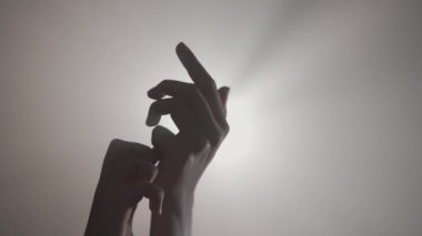 El hareketleri ve işaretleri. El hareketlerini gösteren silüet, parlak spot ışıklarına karşı parmaklarını kapatan, stüdyo arka planında izole edilmiş yakın çekim..