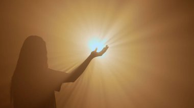 El hareketleri ve işaretleri. Kadın silueti ayakta duruyor ve jest yapıyor. Stüdyonun arka planında izole edilmiş, parlak altın renkli ışığa karşı ışığı yakalıyor..