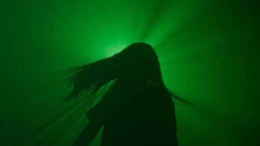 El hareketleri ve işaretleri. Uzun saçlı, siluetli, gece kulübünde dans eden, parlak yeşil ışıklı, stüdyo arka planında izole bir kadın..