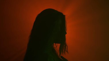 El hareketleri ve işaretleri. Kadın yeşil renkli, koyu renk siluet. Profilde kameranın önünde duruyor. Stüdyonun arka planında parlak kırmızı spot ışığına karşı..