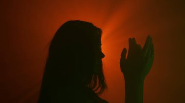 El hareketleri ve işaretleri. Yeşil renkli, neon renkli, koyu renk siluet. Profilde kameranın önünde duran elleri parlak kırmızı spot ışıklarına bakıyor. Stüdyo arka planında izole edilmiş..