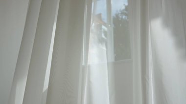 Evde şeffaf tül perdeleri olan pencereler. Şeffaf beyaz ipekten yumuşak kumaşlar açık pencereden süzülüyor, gölgeler tekstil yüzeyine yansıyor..