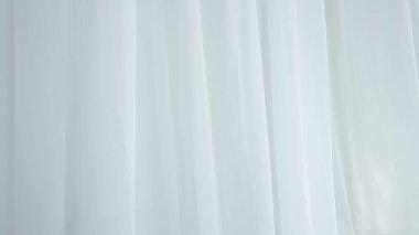 Evde şeffaf tül perdeleri olan pencereler. Şeffaf beyaz ipekten yumuşak kumaşlar güneş ışığı altında yüzüyor, gölgeler tekstil yüzeyine yansıyor, kapanıyor..