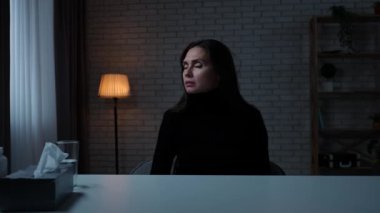 Karanlık dairede depresif bir kadın. Akıl sağlığı sorunları çeken bir kadın, kameranın önünde masada oturuyor, korkmuş bir ifade, sesler duyuyor, şüpheli bir şekilde etrafına bakıyor..